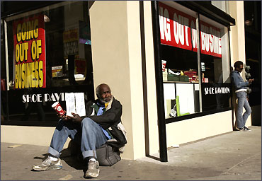 A man holds a sign asking for assistance outside a Shoe Pavilion store that is going out of business in San Francisco.