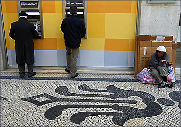 A man begs for money beside people using automated teller machines in downtown Lisbon.