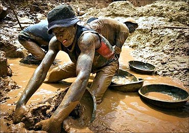 A gold miner scoops mud while digging an open pit at the Chudja mine in the Kilomoto concession.