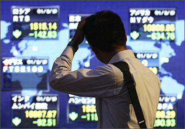 A man scratches his head in front of an electronic board displaying falls in major market indices.