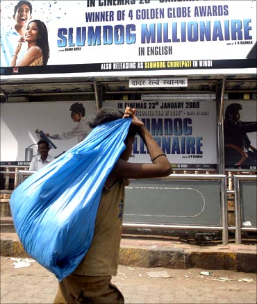 A ragpicker walks past a billboard of the film Slumdog Millionaire at a bus station in Mumbai.