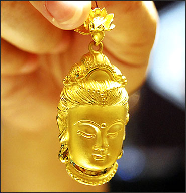 A sales assistant displays a gold accessory in the shape of Buddhist goddess Guanyin.
