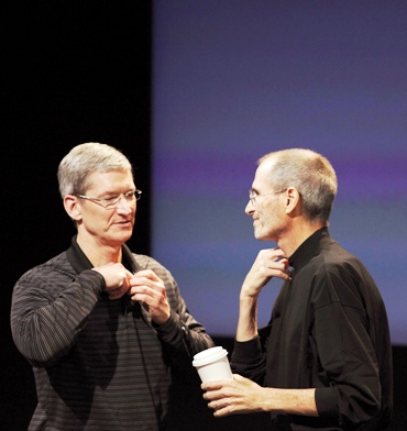 This file photo shows Apple CEO Tim Cook and his predecessor Steve Jobs removing their microphones after a news conference.