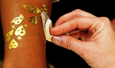 A temporary tattoo design made of gold leaf is placed on a customer's arm at a jewellery shop.