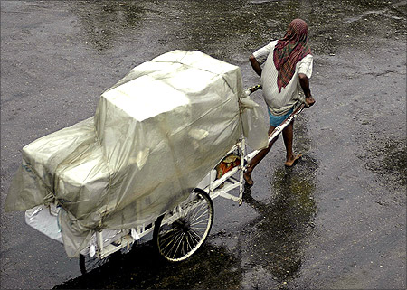 A labourer pulls his handcart full of load on a rainy day in Agartala.