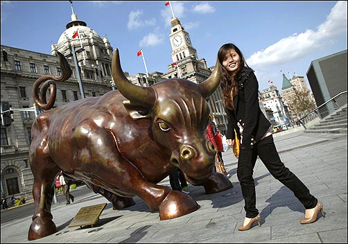 A woman poses next to a bull statue known as the Bund Financial Bull along the Huangpu River in Shanghai.