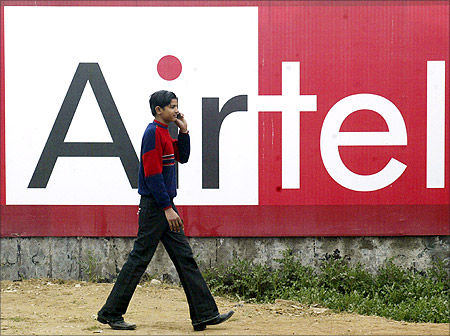 A boy talks on a mobile phone as he walks past a billboard of Bharti Airtel.