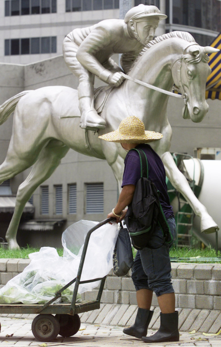 A cleaner pushes his cart past a statue outside the Hong Kong Jockey Club.