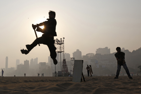A man jumps in the air to hit a ball as he plays cricket in Mumbai.