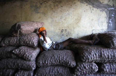 A labourer talks on a mobile phone over sacks of onion at a wholesale market in Mumbai.