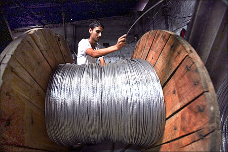 A man rolls electrical power lines onto a wooden wheel at a factory in the outskirts of Jammu.