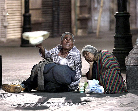 Homeless people sit on the pavement as they wait to receive handouts in Mexico City's historic Zocalo Square.