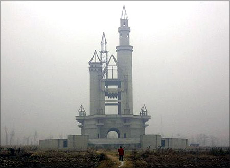 A farmer carries a shovel over his shoulder as he walks to tend his crops in a field that includes an abandoned building, that was to be part of an amusement park called Wonderland.