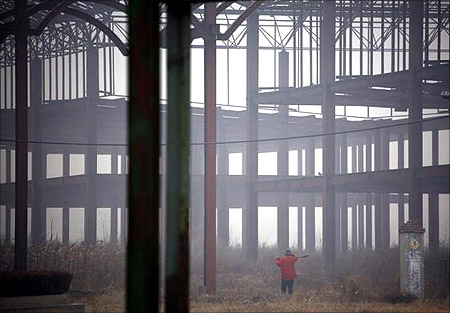 A farmer carries a shovel over his shoulder as he walks through an abandoned building, that was to be part of an amusement park called 'Wonderland', to tend his crops on the outskirts of Beijing.