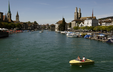 People sit in a boat on the Limmat River during sunny summer weather in Zurich.
