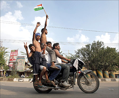 Supporters of veteran Indian social activist Anna Hazare ride on a motorcycle holding an Indian national flag.