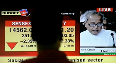 A stockbroker watches a news channel screen, showing Indian Finance Minister Pranab Mukherjee.