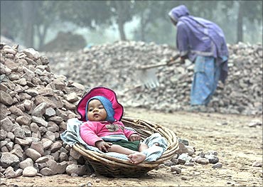 Five-month-old Roshni, child of a woman labourer (R), rests in a basket at a roadside construction site.