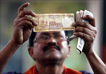 A worker at a fuel station checks a 500 Indian rupee note after filing a vehicle with fuel.