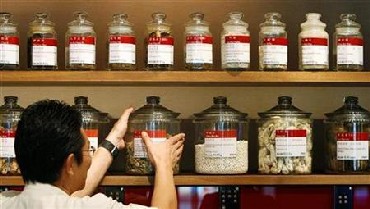 A shop assistant arranges jars containing roots and herbs at a Chinese medicine shop.