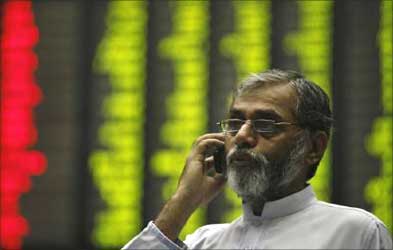 A man talks on a mobile phone near an electronic board displaying stock prices at the Karachi Stock Exchange.