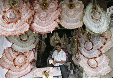 A shopkeeper staples Indian currency notes to make garlands at a market.