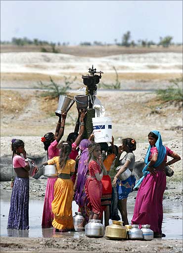 Women fill buckets with drinking water that is leaking from a broken pipeline at Dharji village.