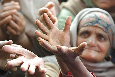 An old lady raises her hands to receive food from a roadside charitable community kitchen.