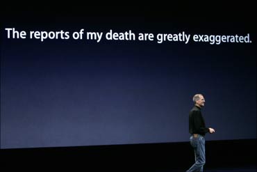 Steve Jobs takes the stage beneath a sign that makes light of reports on his health.
