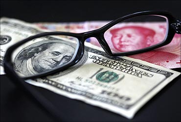 A US dollar note (L) and a Chinese Yuan banknote are seen through a pair of spectacles.