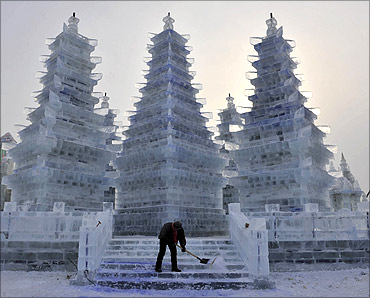 A worker cleans an ice sculpture of pagodas prior to the Harbin International Ice and Snow Festival