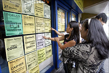 Applicants look at job offers displayed on a glass window of a recruitment agency in Manila.