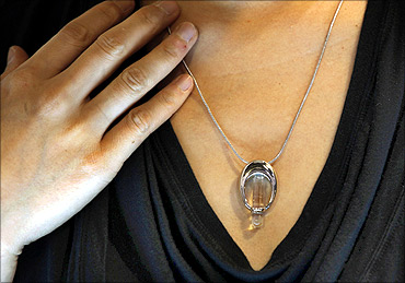 An exhibitor poses with a DNA necklace, a locket made by a Hong Kong co containing DNA of a person.