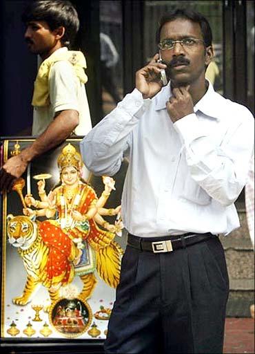 Image: A man speaks on a his mobile as he looks at a large screen displaying India's benchmark share index. Photographs: Arko Datta/Reuters.