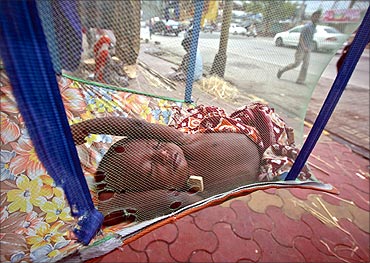 Five-month-old Rahul sleeps in a hammock next to shop along a sidewalk in Mumbai.