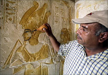 A worker blows dust off a mural in one of six tombs in the New Kingdom Cemetery in South Saqqara.