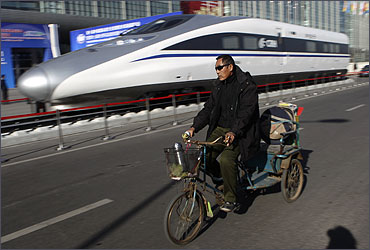 A Chinese resident rides a tricycle past the head of a CRH Harmony bullet train.