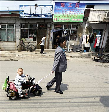 A woman pulls a toy ride carrying her grandson in a residential area for migrant workers.