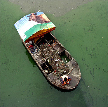 Workers on a boat collect trash from a polluted waterway in Beijing.