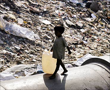 A boy carries a plastic container to fill water past a garbage dump in Mumbai.