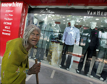 A beggar walks past a shop window.