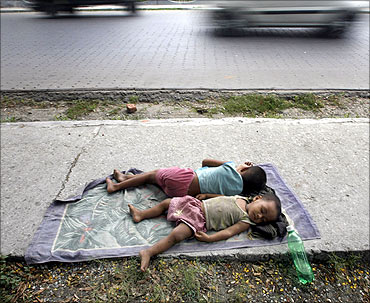 Homeless children sleep on the pavement beside a busy road.