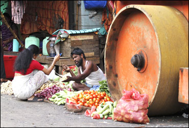 A vendor sells vegetables to a customer next to a parked road roller on a roadside in Kolkata.