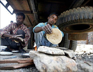 Labourers make roti under a truck at a roadside in Noida.