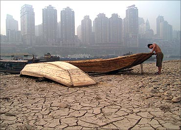 A boatman repairs his boat on the dried-up riverbed of the Jialing River.