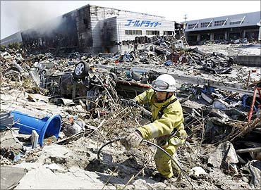 A firefighter walks around rubble near a burning factory damaged by an earthquake.