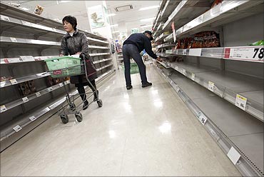 People shop for food from almost empty shelves at a big-box supermarket in Tokyo.