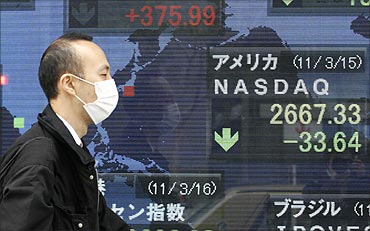 A man wearing a mask walks past an electronic board displaying the Nasdaq average.