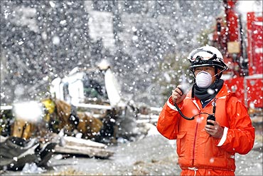 A rescue worker uses a two-way radio transceiver during heavy snowfall at a factory area.