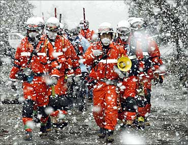 Rescue workers walk in heavy snowfall at a factory area that was devastated by earthquake.